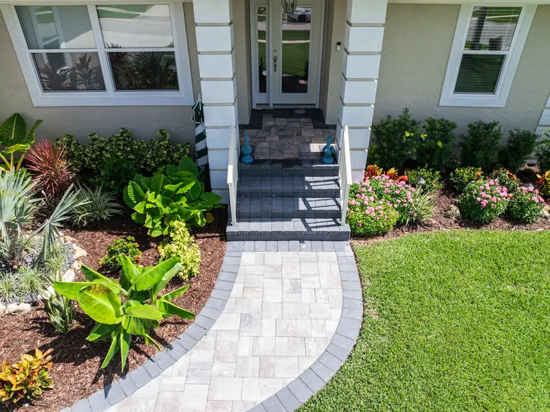 Paver walkway to a front porch flanked by banana plants and pink flowering shrubs