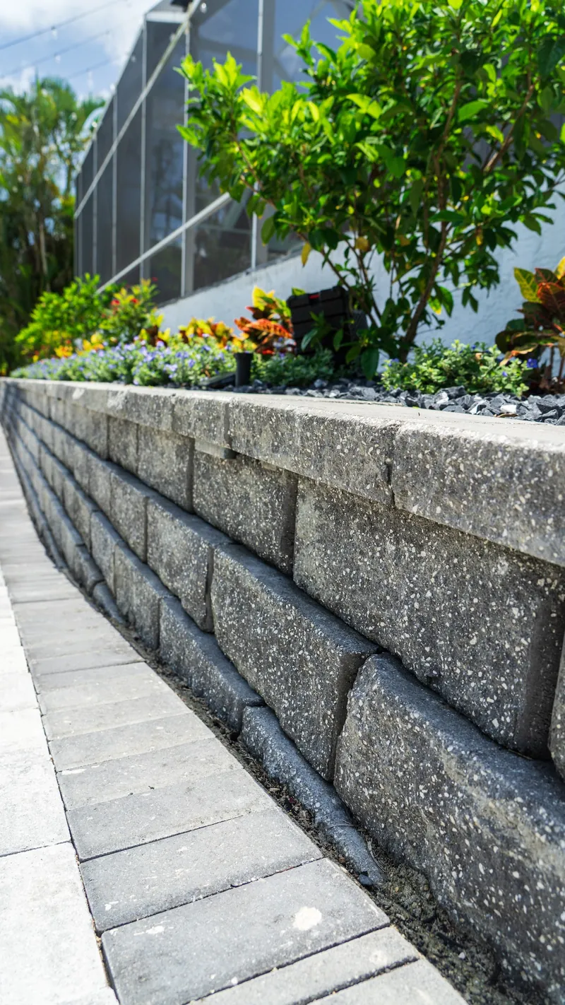 Gray block retaining wall beside a light paver walkway with a raised planting bed above