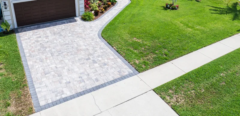 Light blended paver driveway with a charcoal soldier-course border connecting to a curved paver walkway