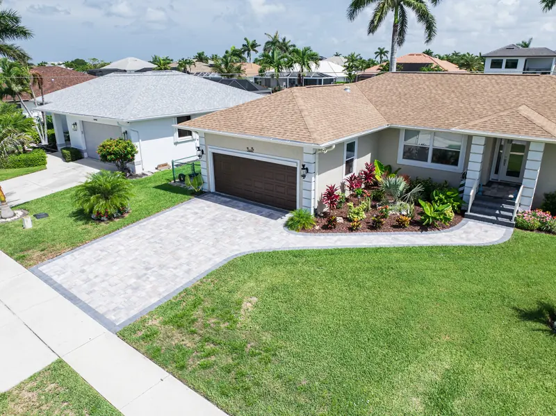 Front yard with a full green lawn, paver driveway and colorful foundation beds