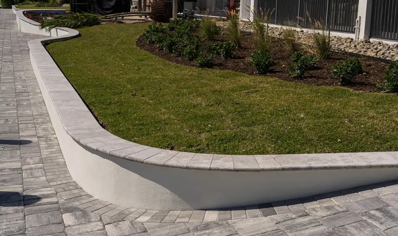 Fresh green lawn inside a curved raised planting area beside pavers